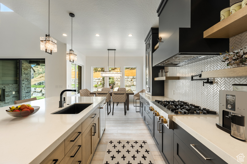 Kitchen featuring open shelves, a sink, premium range hood, light countertops, and decorative backsplash
