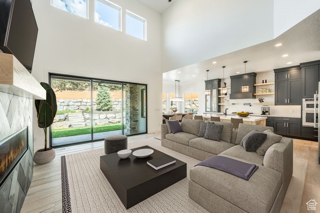 Living room with a towering ceiling, healthy amount of natural light, light wood-style floors, a glass covered fireplace, and recessed lighting