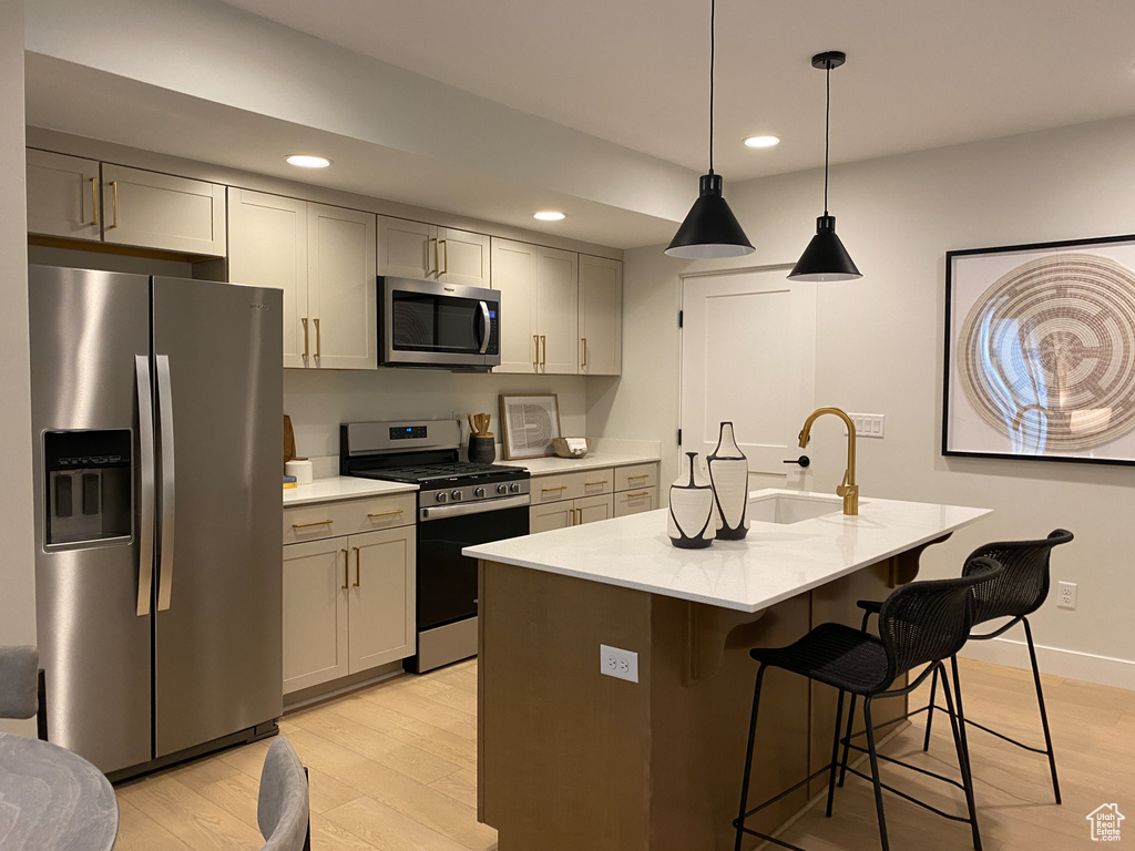 Kitchen with recessed lighting, stainless steel appliances, a sink, a kitchen bar, and light wood-style flooring