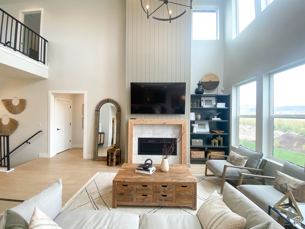 Living room featuring a high ceiling, wood finished floors, baseboards, a fireplace, and a notable chandelier