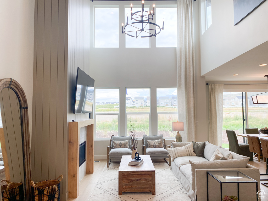 Living area with light wood finished floors, a glass covered fireplace, a towering ceiling, and a notable chandelier