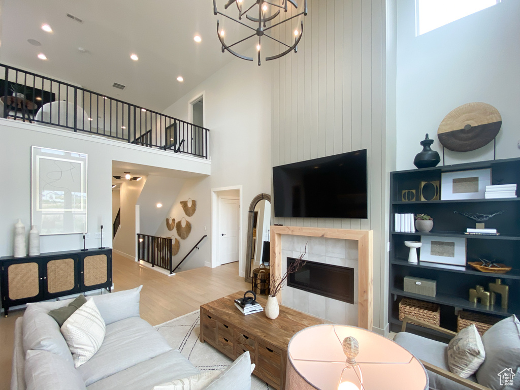 Living room with light wood finished floors, a tiled fireplace, a towering ceiling, and recessed lighting