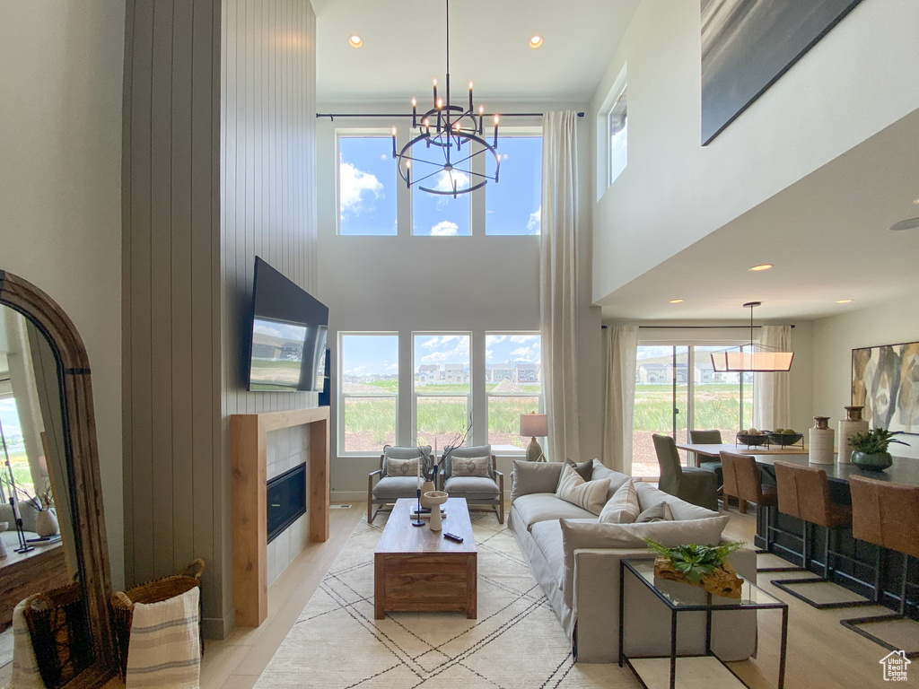 Living area featuring recessed lighting, a tile fireplace, a high ceiling, a chandelier, and light wood-style flooring