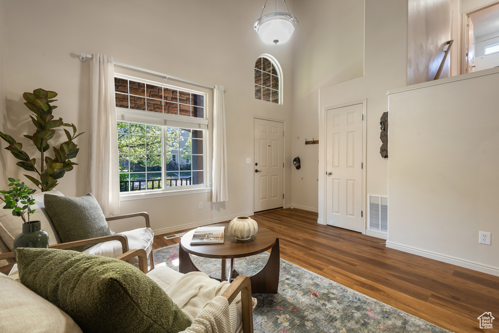 Living area with wood finished floors, visible vents, baseboards, and a high ceiling