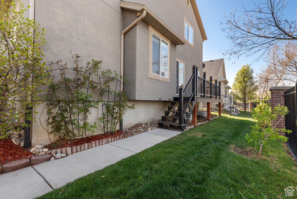 View of side of property featuring stucco siding, fence, stairs, and a lawn