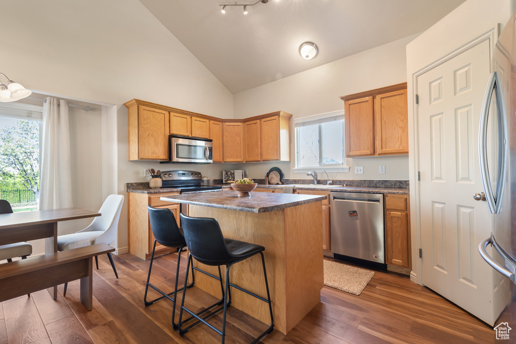 Kitchen featuring dark countertops, a center island, a kitchen breakfast bar, stainless steel appliances, and dark wood-style flooring