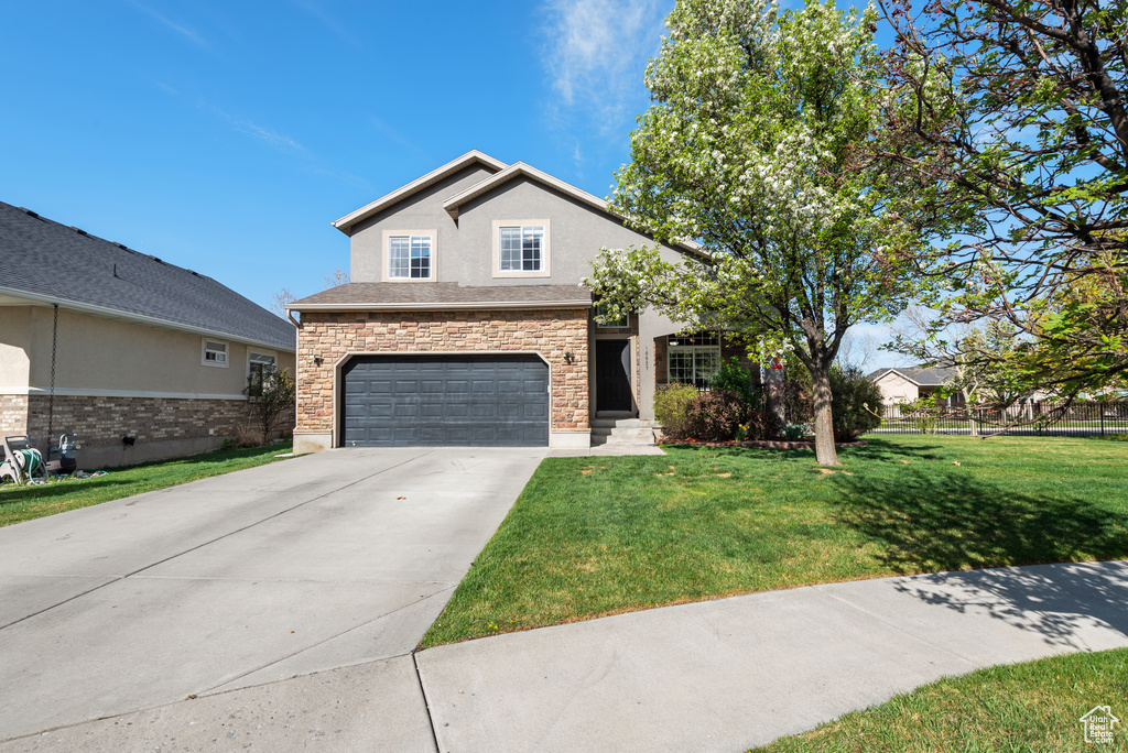 Traditional-style home featuring an attached garage, driveway, stone siding, and a front lawn