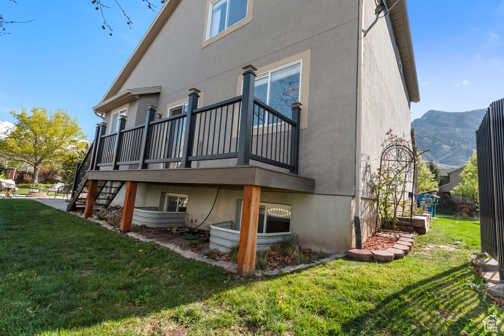 Rear view of property featuring stucco siding, a deck with mountain view, a yard, and stairs