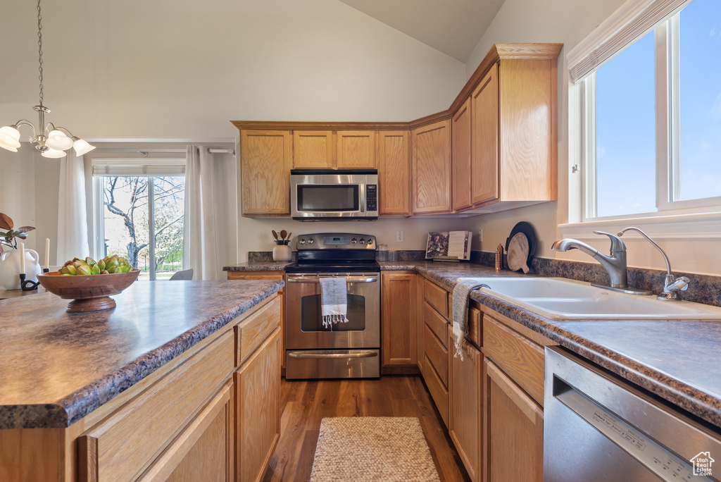 Kitchen with stainless steel appliances, a sink, dark countertops, lofted ceiling, and dark wood-type flooring