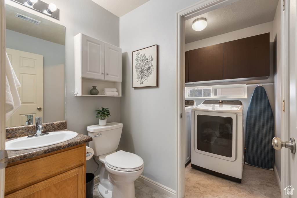 Half bathroom with toilet, baseboards, visible vents, vanity, and washer / dryer