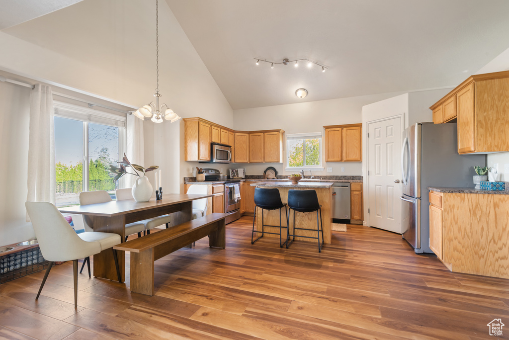 Dining area with high vaulted ceiling, a notable chandelier, and wood finished floors
