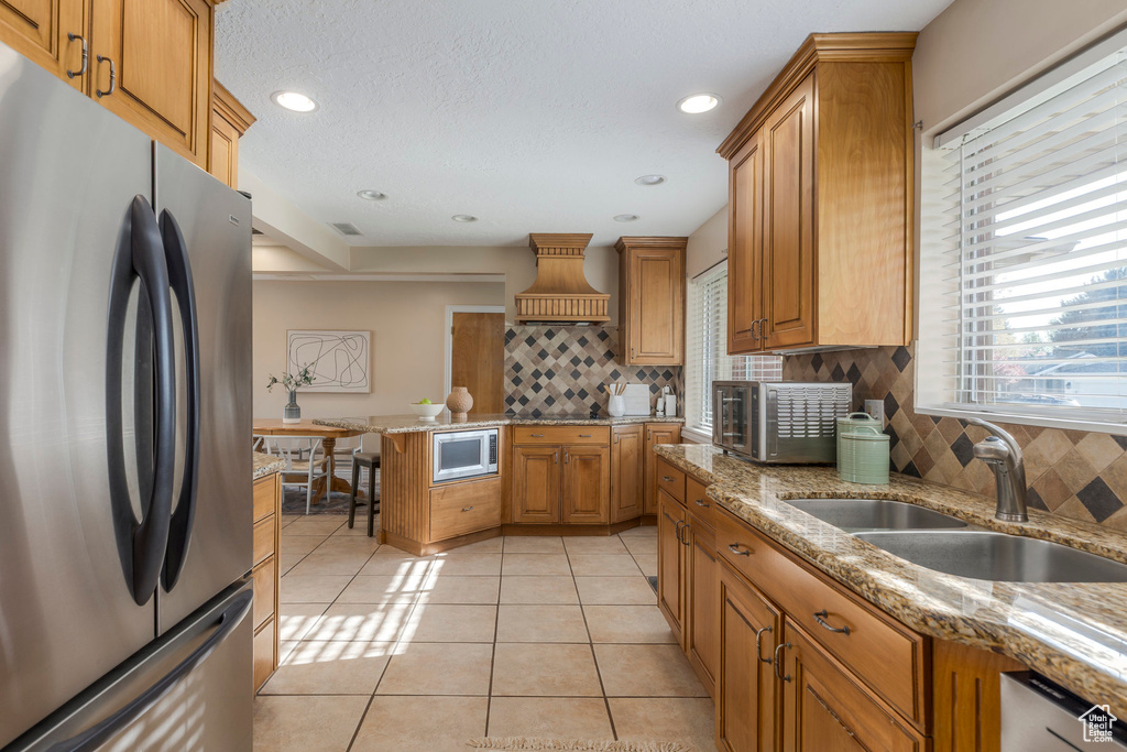 Kitchen with appliances with stainless steel finishes, a sink, backsplash, custom exhaust hood, and light tile patterned floors