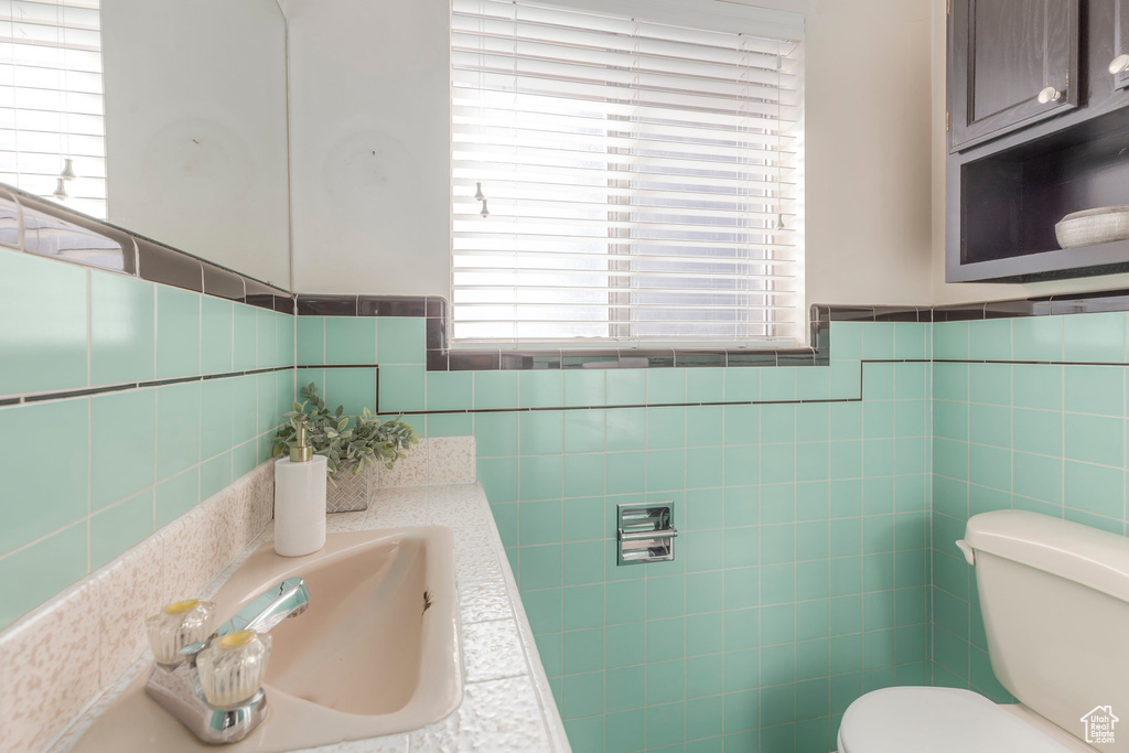 Bathroom with tile walls, toilet, plenty of natural light, vanity, and a wainscoted wall
