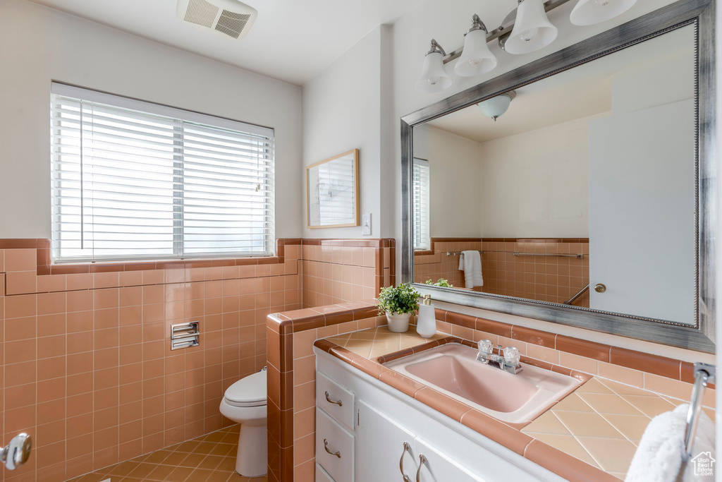 Bathroom featuring tile walls, toilet, vanity, wainscoting, and tile patterned floors
