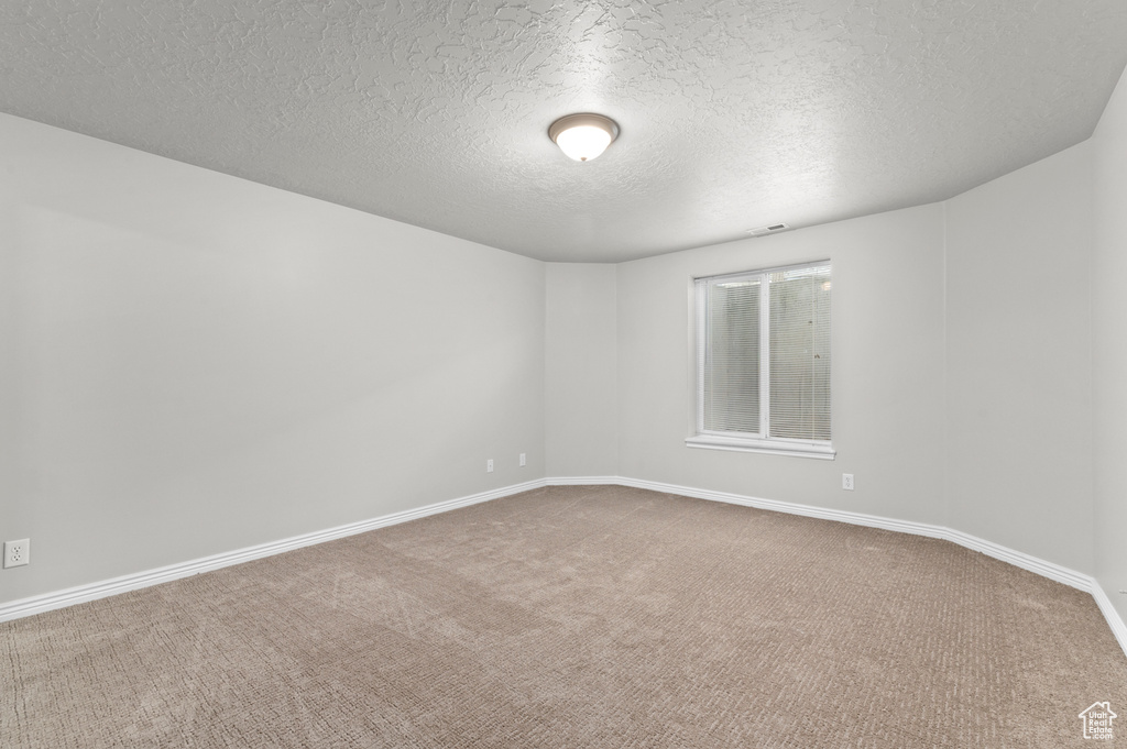 Spare room featuring baseboards, a textured ceiling, visible vents, and carpet