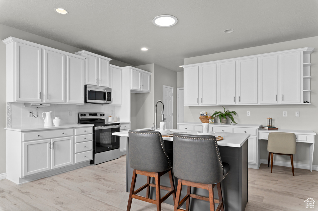 Kitchen with white cabinets, a kitchen breakfast bar, light countertops, light wood-style floors, and appliances with stainless steel finishes