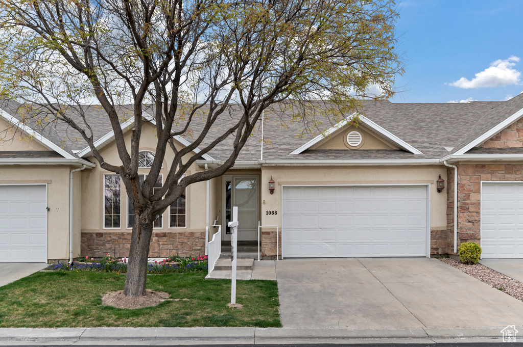 Townhome / multi-family property with driveway, stone siding, a front yard, and stucco siding