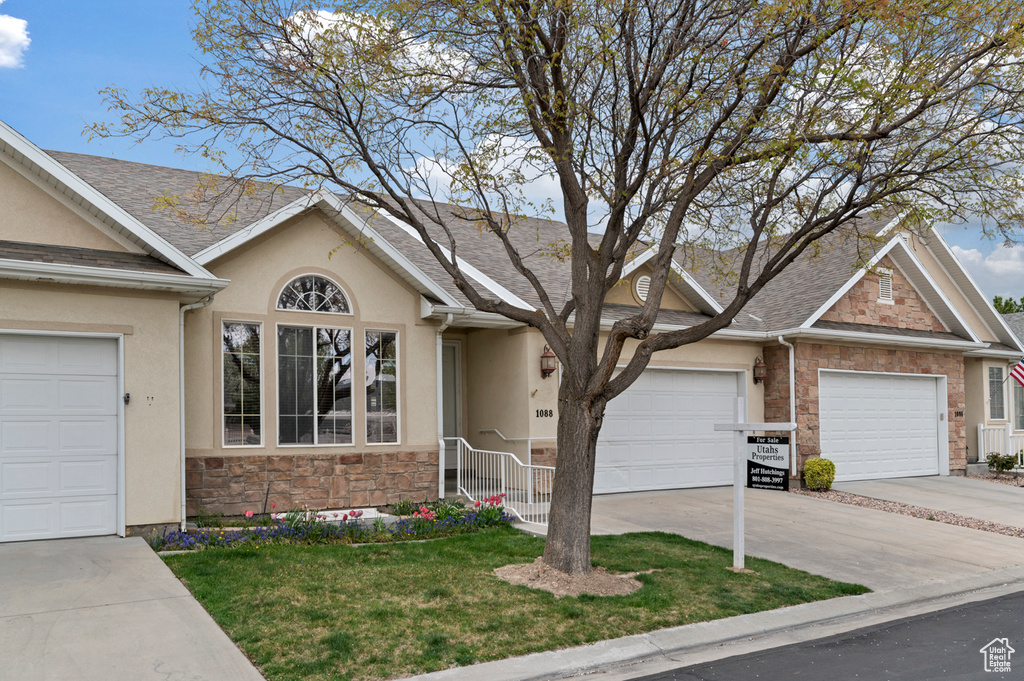 Ranch-style home with a front lawn, stone siding, concrete driveway, a garage, and stucco siding