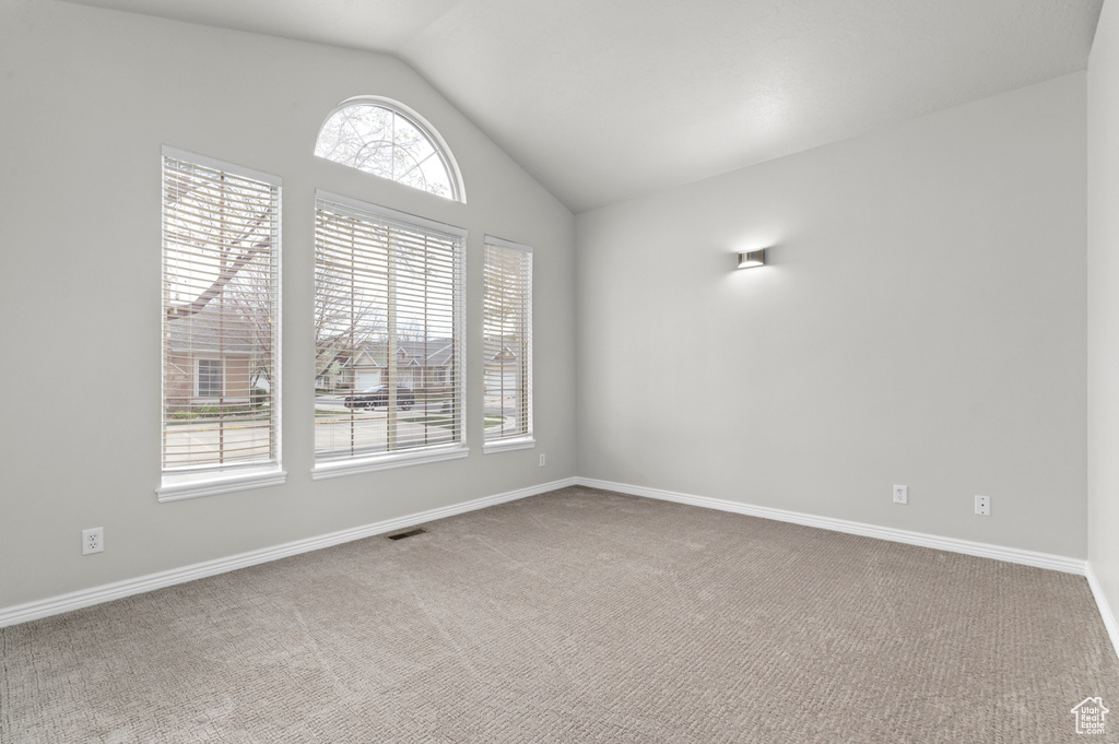 Carpeted spare room featuring a wealth of natural light, lofted ceiling, visible vents, and baseboards