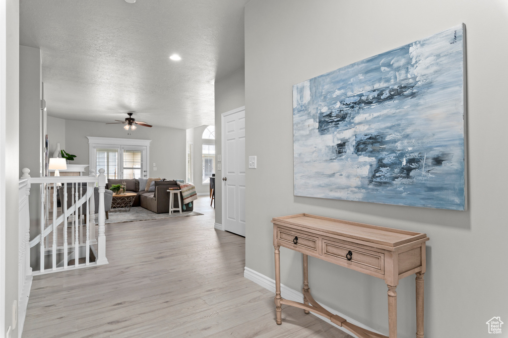 Hall featuring light wood-type flooring, baseboards, a textured ceiling, and an upstairs landing