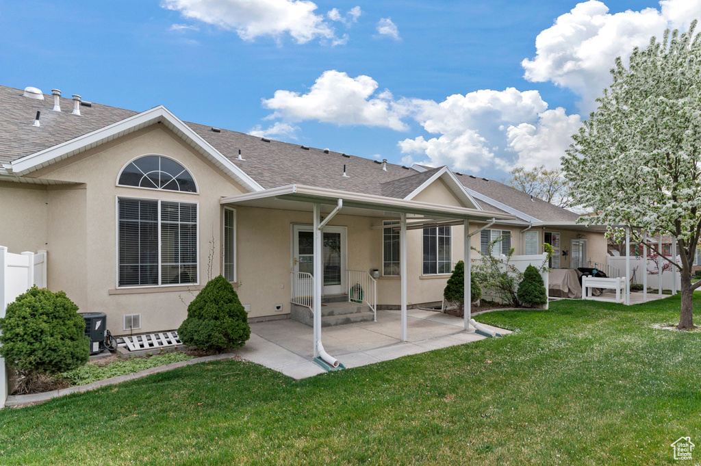 Back of house featuring stucco siding, a patio area, a shingled roof, and a lawn