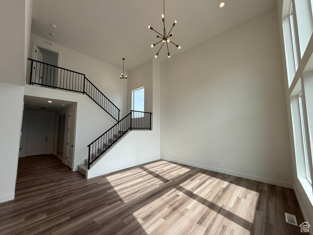 Unfurnished living room with a high ceiling, a chandelier, wood finished floors, stairs, and baseboards