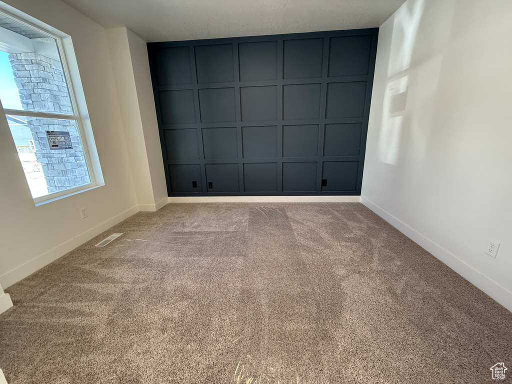 Carpeted empty room featuring baseboards and a decorative wall