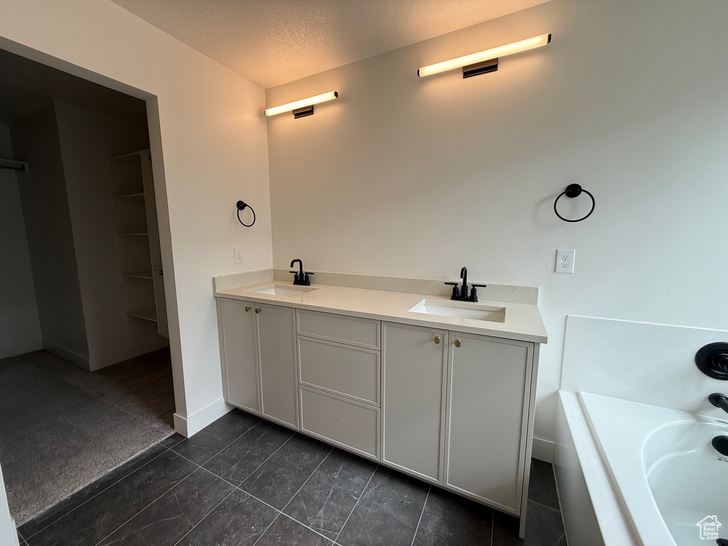 Bathroom featuring a tub to relax in, double vanity, a textured ceiling, and baseboards