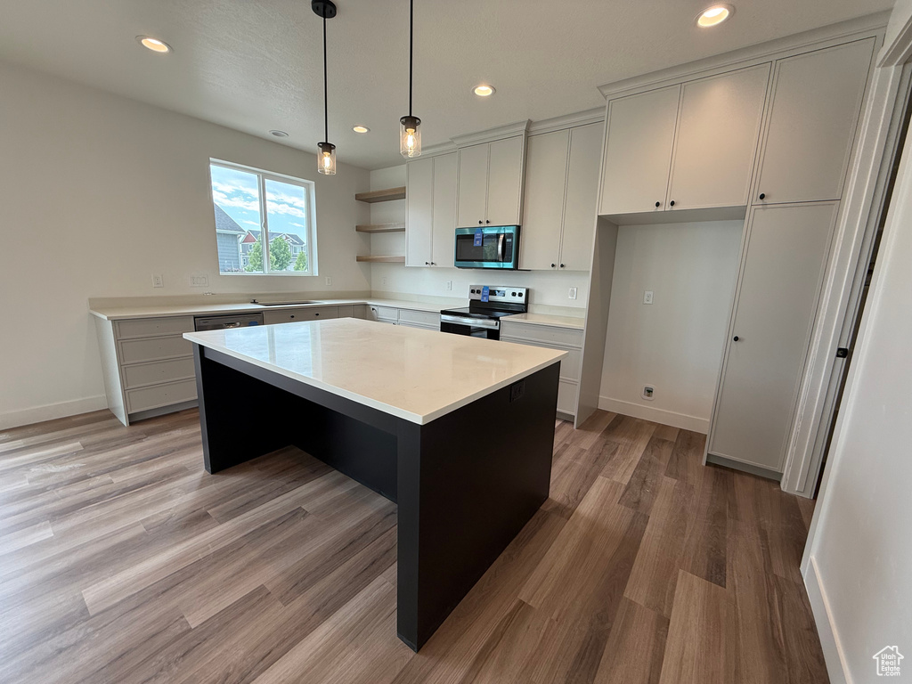 Kitchen with appliances with stainless steel finishes, open shelves, light countertops, light wood-style floors, and a center island