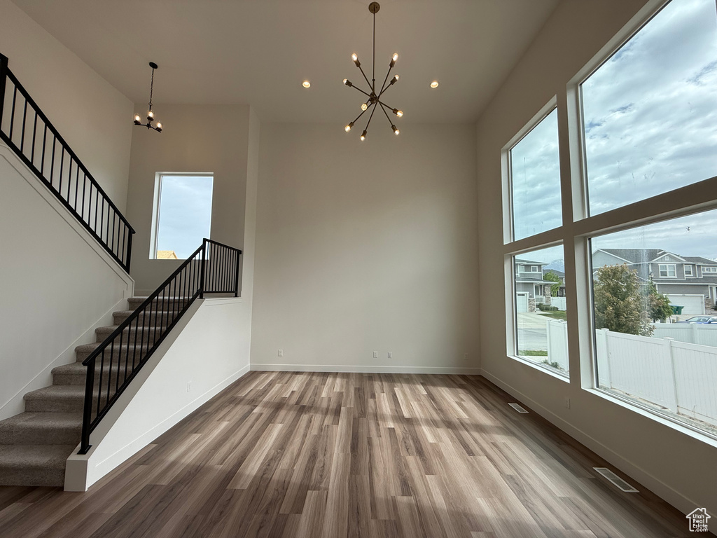 Unfurnished living room with a chandelier, wood finished floors, stairs, baseboards, and recessed lighting
