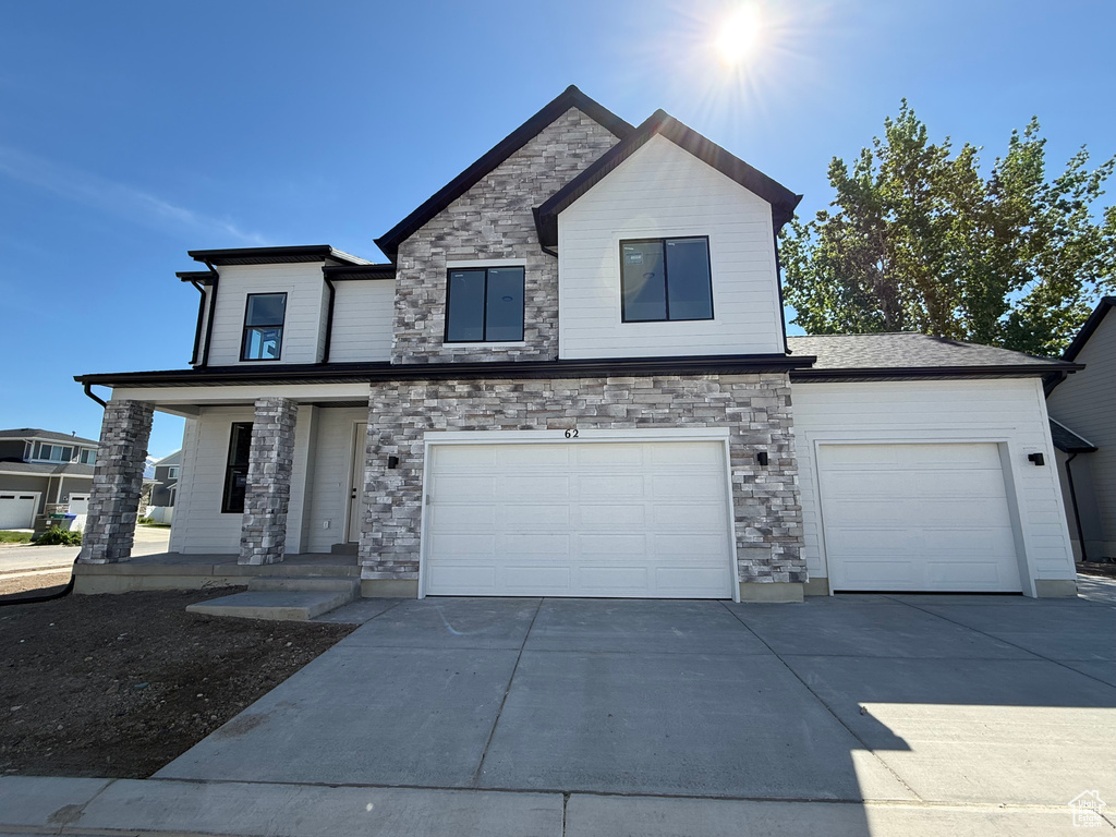 View of front facade with concrete driveway, stone siding, a garage, and a porch