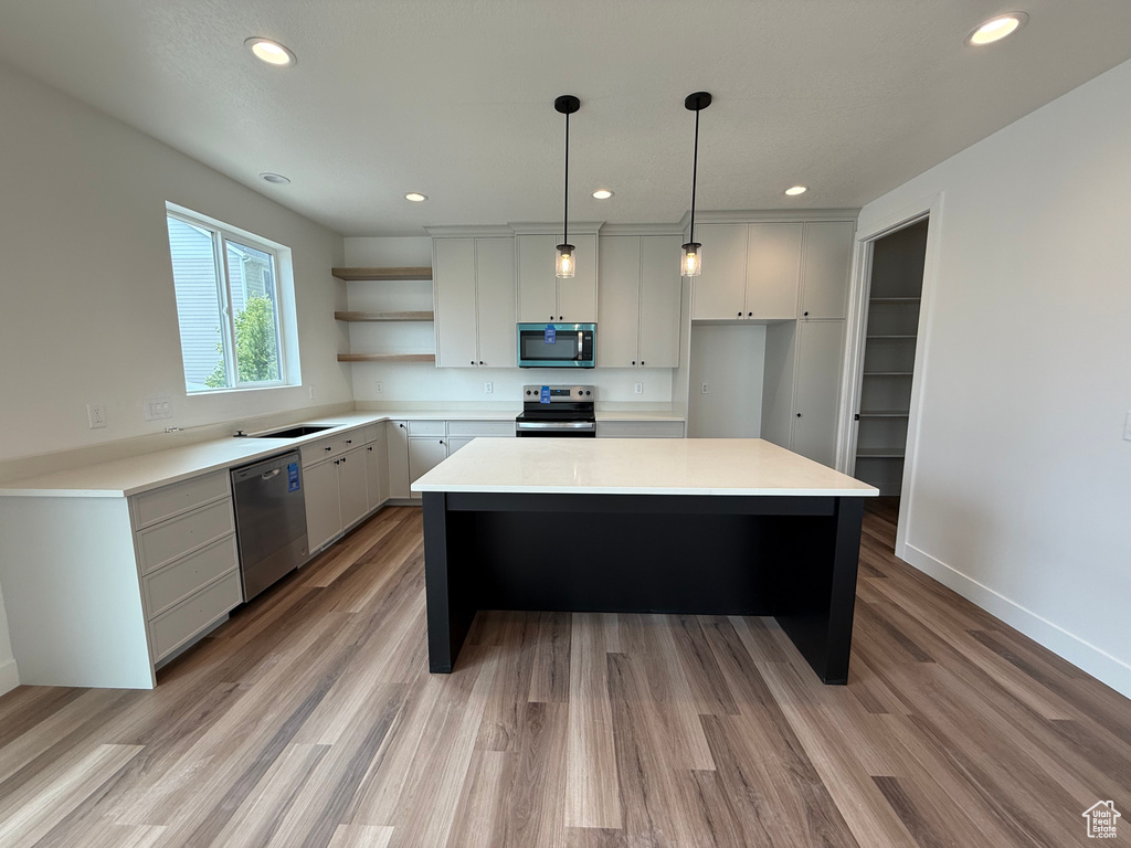 Kitchen with appliances with stainless steel finishes, open shelves, recessed lighting, light countertops, and a kitchen island