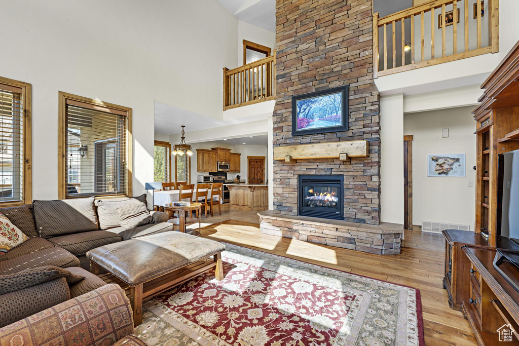 Living room featuring visible vents, a high ceiling, a stone fireplace, a chandelier, and light wood-style floors