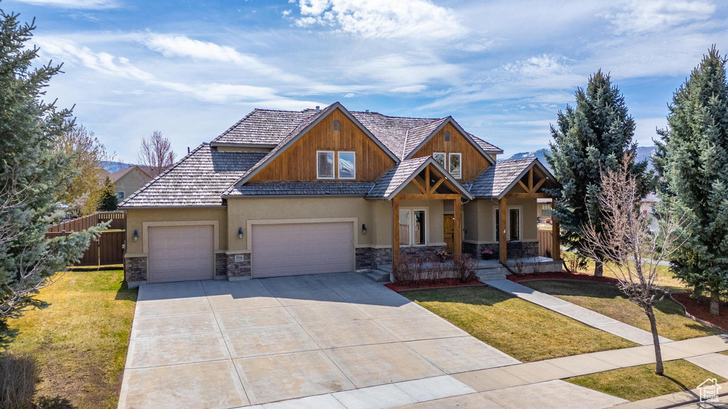 Craftsman-style home featuring a front lawn, stone siding, concrete driveway, fence, and an attached garage