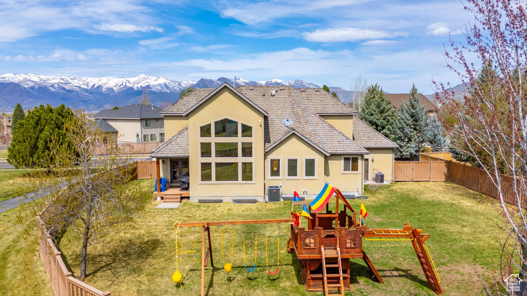 Rear view of house with a mountain view, a fenced backyard, a playground, and stucco siding