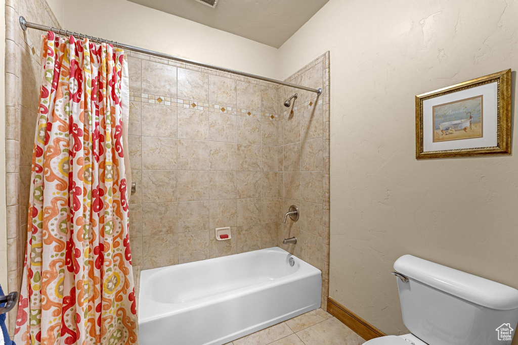 Full bathroom with tile patterned floors, shower / tub combo with curtain, baseboards, and toilet