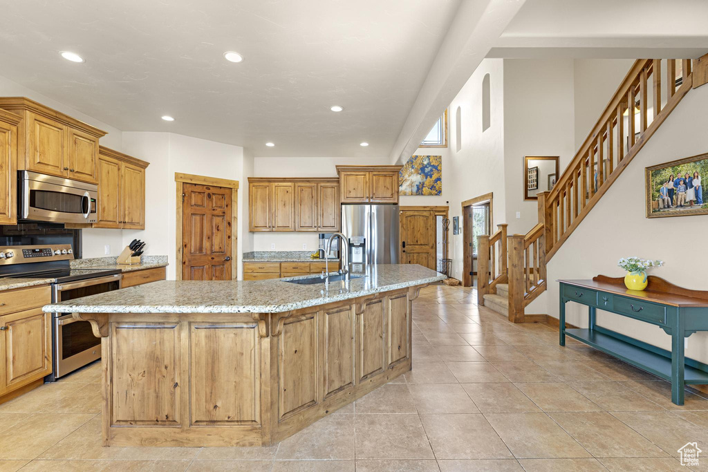 Kitchen with light stone counters, recessed lighting, a center island with sink, stainless steel appliances, and a sink