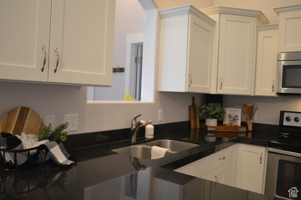 Kitchen featuring arched walkways, appliances with stainless steel finishes, a sink, and white cabinetry