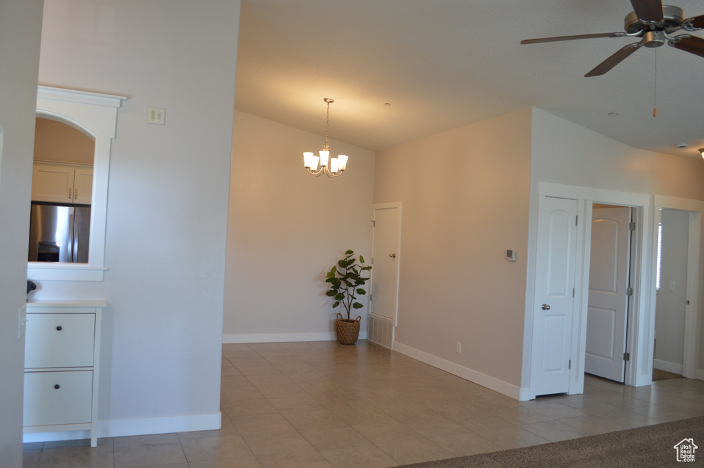 Unfurnished room with arched walkways, light tile patterned floors, ceiling fan with notable chandelier, and baseboards