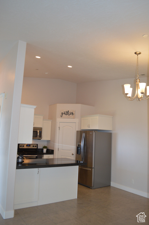 Kitchen featuring an inviting chandelier, dark countertops, appliances with stainless steel finishes, a peninsula, and white cabinetry