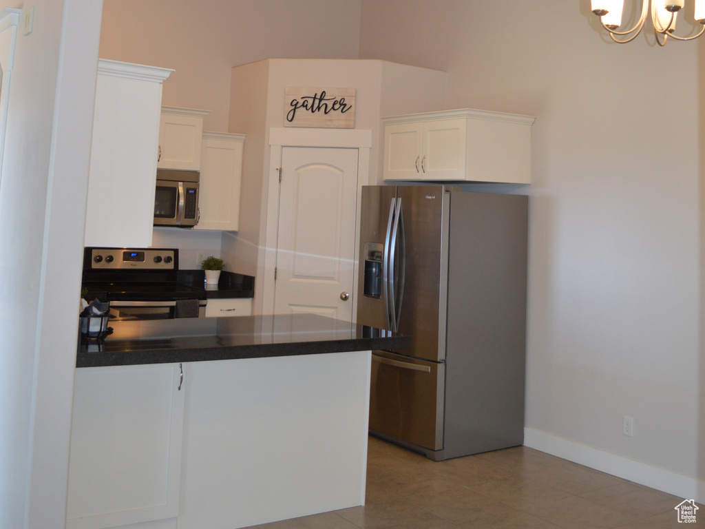 Kitchen featuring an inviting chandelier, dark countertops, appliances with stainless steel finishes, a peninsula, and white cabinetry