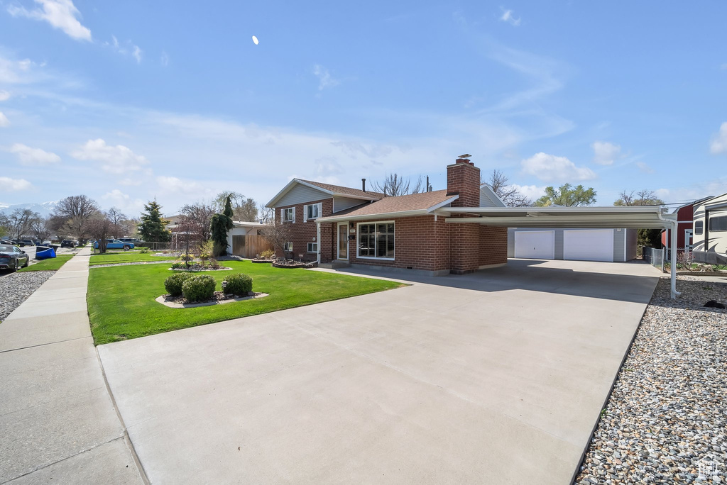 Tri-level home with driveway, brick siding, a front yard, and a chimney