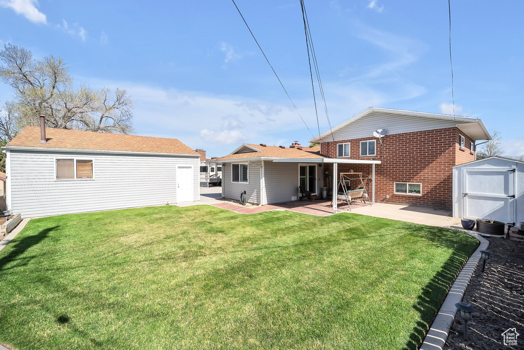 Rear view of property featuring an outbuilding, brick siding, a lawn, a shed, and a patio