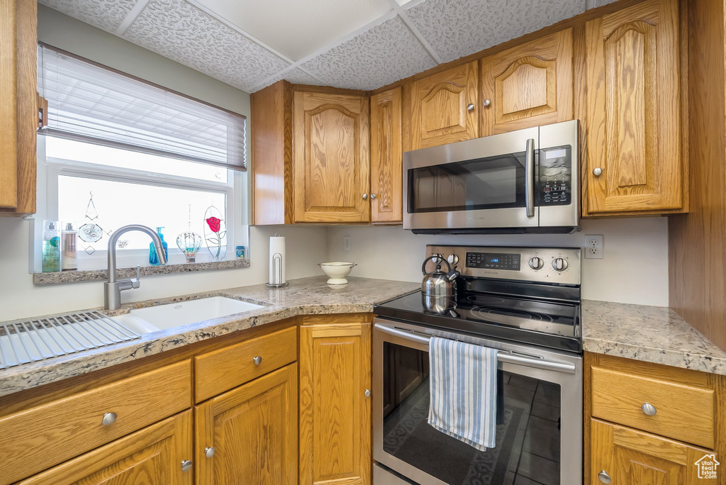 Kitchen with light countertops, brown cabinetry, stainless steel appliances, and a sink