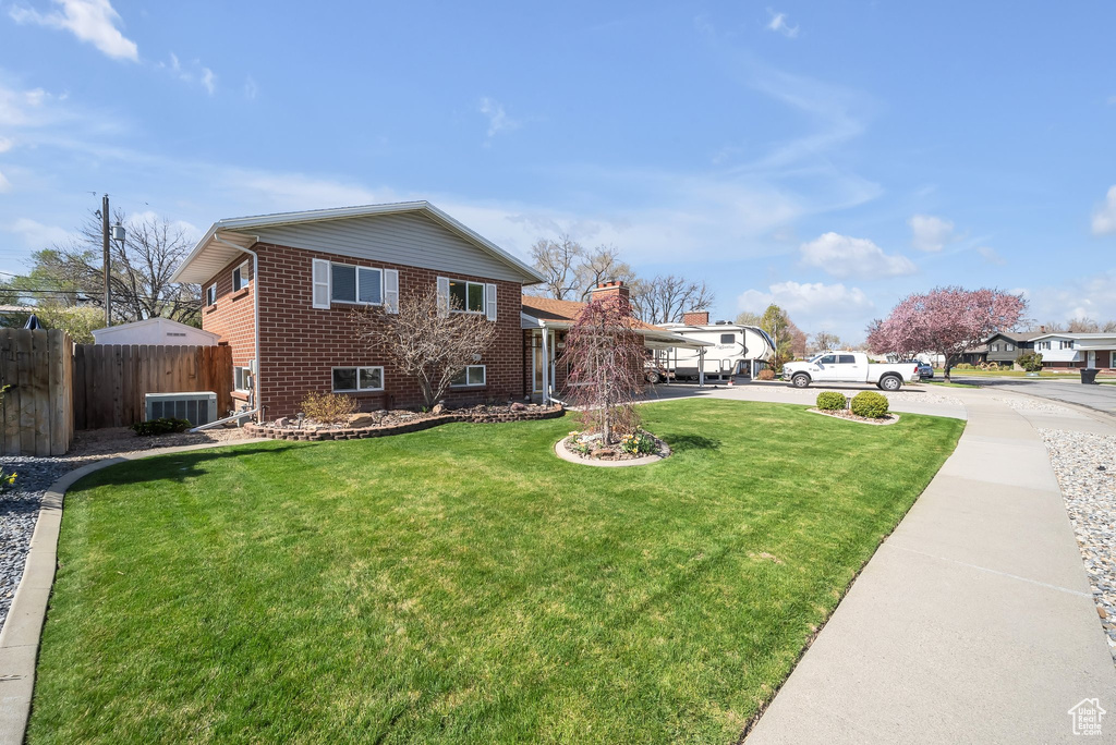 View of front of home with brick siding, driveway, a front lawn, and fence