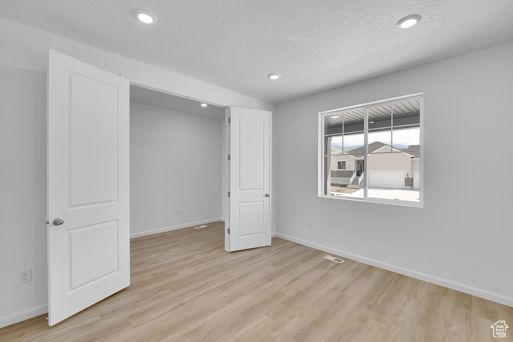 Spare room with light wood-style floors, baseboards, recessed lighting, and a textured ceiling