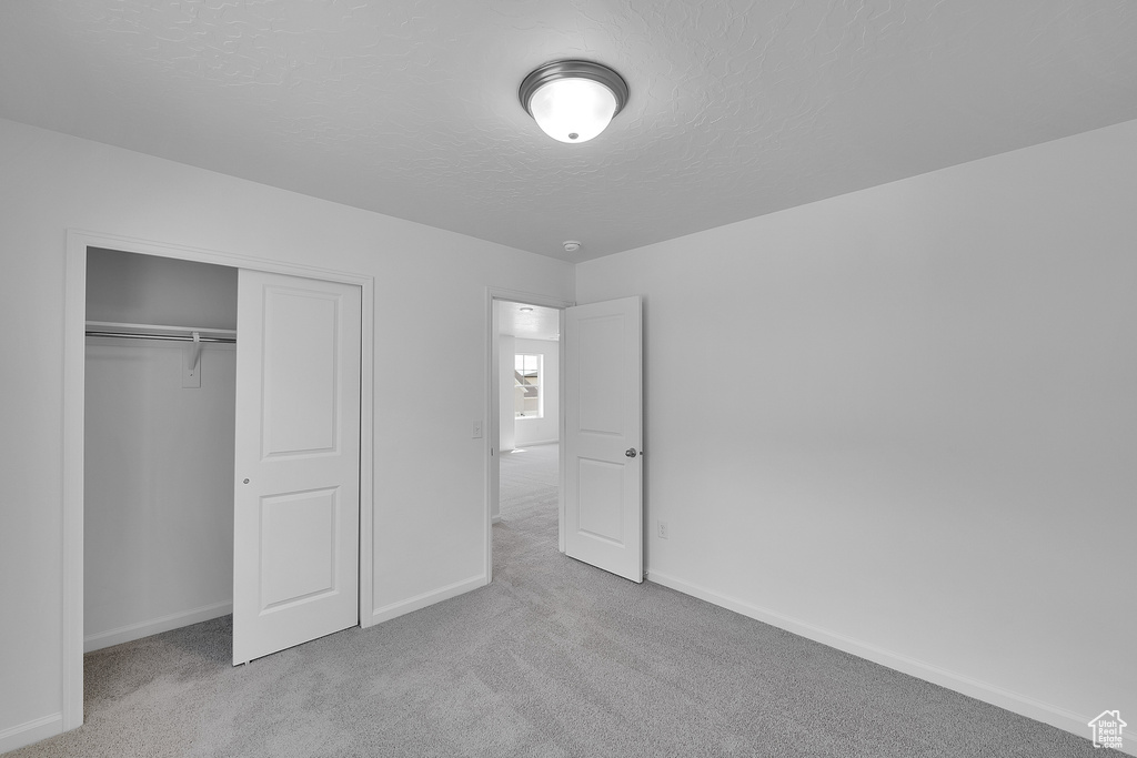 Unfurnished bedroom featuring carpet, baseboards, a textured ceiling, and a closet