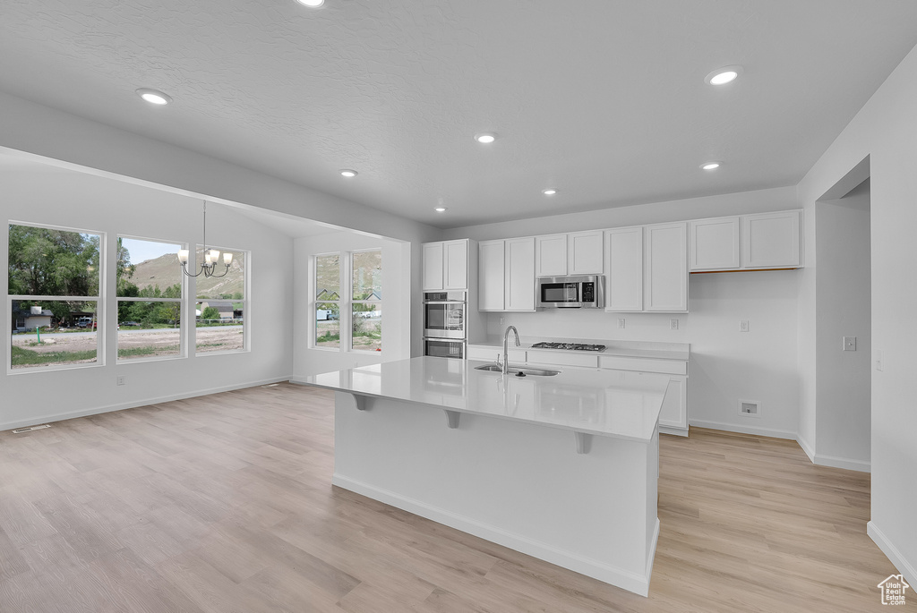 Kitchen with a sink, appliances with stainless steel finishes, white cabinetry, light wood-style flooring, and baseboards