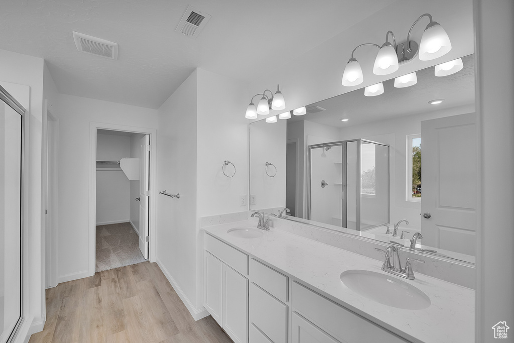 Bathroom featuring a shower stall, a spacious closet, double vanity, wood finished floors, and baseboards