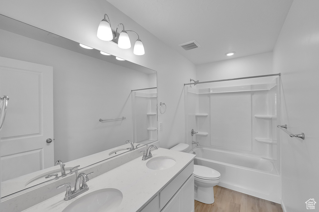 Full bath with toilet, double vanity, washtub / shower combination, wood finished floors, and recessed lighting